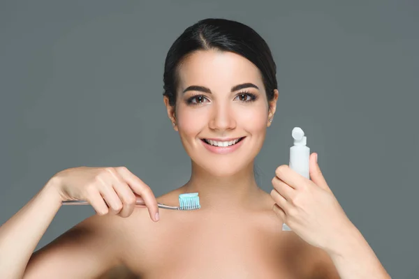 Portrait de femme souriante avec brosse à dents et tube de pâte dentaire dans les mains isolées sur gris — Photo de stock