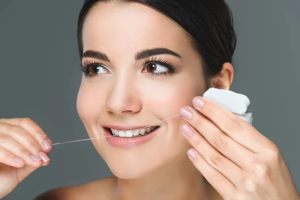 Portrait of smiling woman with beautiful white teeth and dental floss isolated on grey — Stock Photo