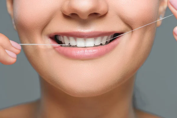 Vue partielle de la femme souriante avec de belles dents blanches et fil dentaire isolé sur gris — Photo de stock