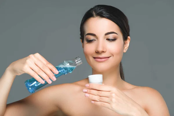 Portrait of smiling woman with bare shoulders holding mouthwash isolated on grey — Stock Photo