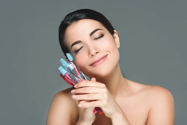 Portrait of beautiful woman holding tooth brushes isolated on grey — Stock Photo