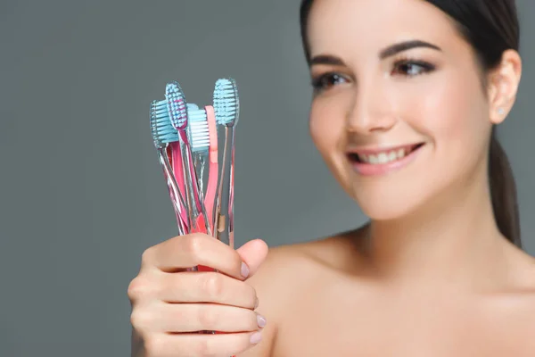 Portrait of beautiful woman holding tooth brushes isolated on grey — Stock Photo