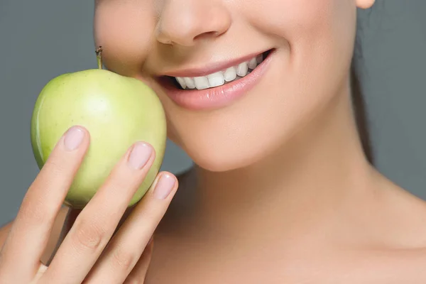 Частичный взгляд женщины с белыми зубами и свежим яблоком, изолированным на сером — стоковое фото