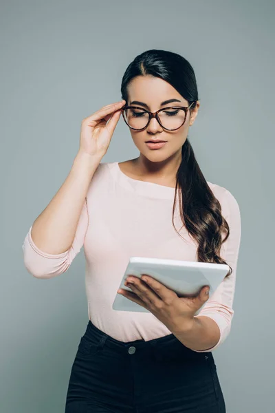 Portrait of brunette woman in eyeglasses using digital tablet isolated on grey — Stock Photo
