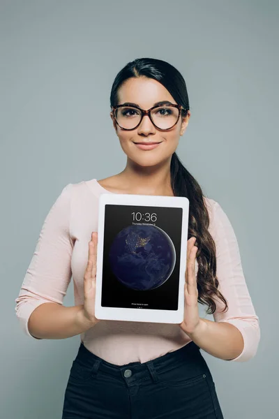 Jolie femme en lunettes montrant comprimé ipad, isolé sur gris — Photo de stock