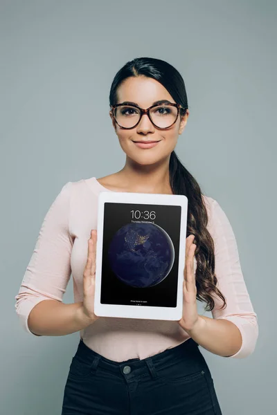 Attractive woman in eyeglasses showing ipad tablet, isolated on grey — Stock Photo