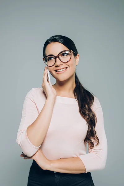 Beautiful smiling woman in eyeglasses talking on smartphone, isolated on grey — Stock Photo