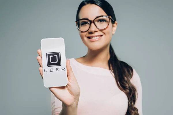 Menina atraente mostrando smartphone com aparelho uber, isolado em cinza — Fotografia de Stock