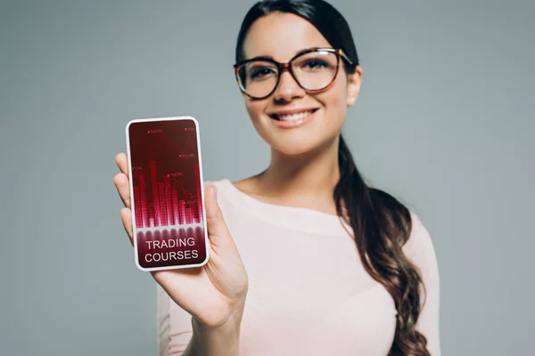 Frau zeigt Smartphone mit Handelskursen, isoliert auf grau — Stockfoto