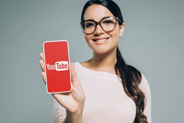 Beautiful smiling girl presenting smartphone with youtube appliance, isolated on grey — Stock Photo