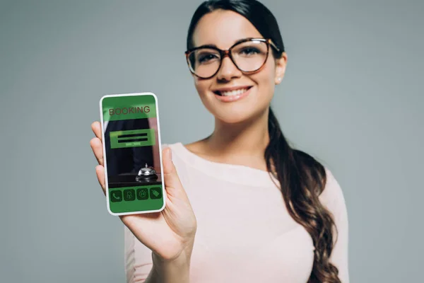 Mujer mostrando teléfono inteligente con aplicación de reserva, aislado en gris - foto de stock