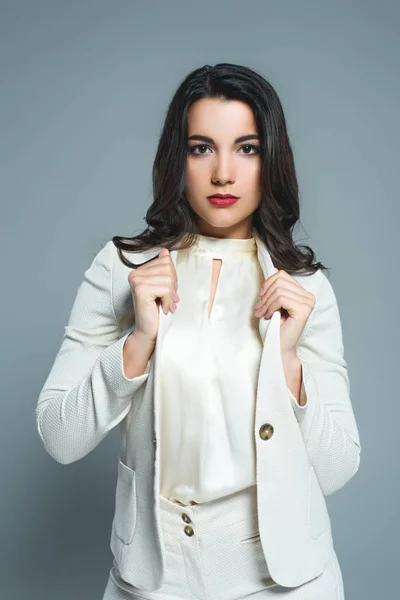 Приваблива брюнетка жінка позує в білому формальному одязі, ізольована на сірому — стокове фото