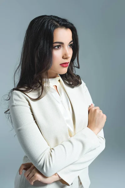 Mulher morena de terno branco posando com braços cruzados, isolada em cinza — Fotografia de Stock