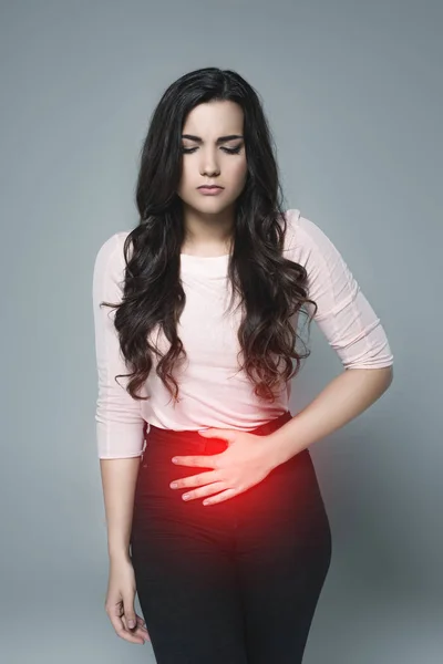 Menina bonita que sofre de dor abdominal com ponto doloroso vermelho, isolado em cinza — Fotografia de Stock