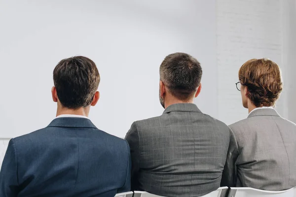 Rear view of three businessmen sitting on chairs during training in hub — Stock Photo