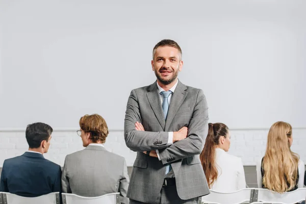 Handsome coach with crossed arms looking at camera during business training in hub — Stock Photo
