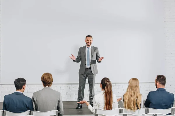 Handsome business coach standing on stage and gesturing during training in hub — Stock Photo