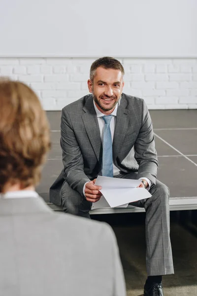 Sonriente apuesto entrenador de negocios sentado en el escenario durante la formación en el centro - foto de stock