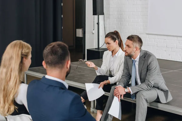 Business trainers sitting on stage with documents in hub — Stock Photo