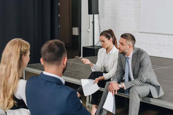 Business-Trainer sitzen mit Dokumenten in der Hand auf der Bühne — Stockfoto