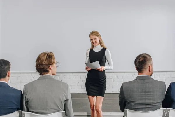 Attractive business coach holding documents during training in hub — Stock Photo