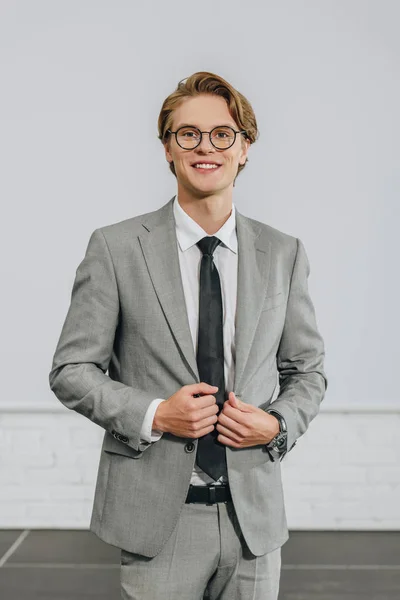 Beau homme d'affaires souriant touchant veste et regardant la caméra en moyeu — Photo de stock