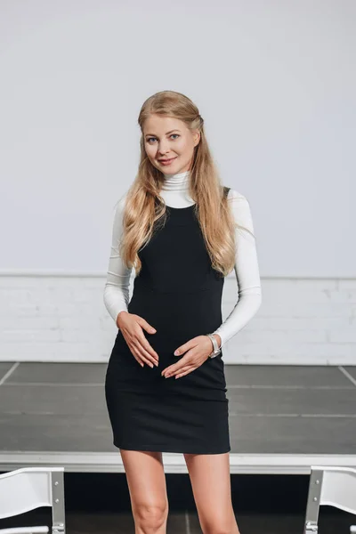 Pregnant businesswoman touching belly and looking at camera in hub — Stock Photo
