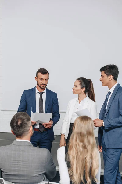 Empresarios serios hablando de documentos durante la formación en el centro - foto de stock