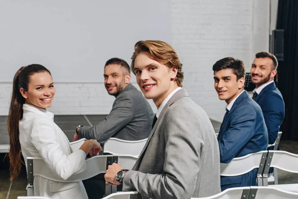Smiling businesspeople sitting on chairs at training in hub and looking at camera — Stock Photo