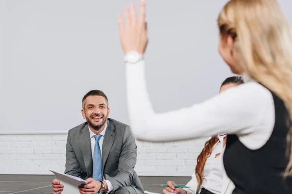 Handsome business coach looking at participant with raised hand during training in hub — Stock Photo