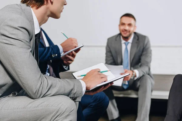 Handsome business coach sitting on stage during training in hub, businessmen holding notebooks — Stock Photo