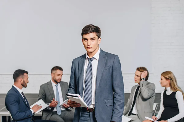 Handsome business coach standing in front of businesspeople at training in hub — Stock Photo