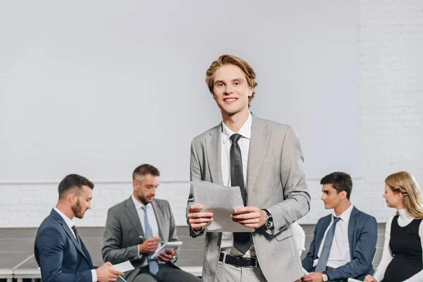 Business coach standing in front of businesspeople at training in hub and looking at camera — Stock Photo