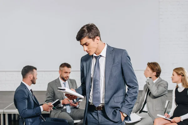 Businesscoach schaut vor Geschäftsleuten beim Training in Hub auf das Notizbuch — Stockfoto