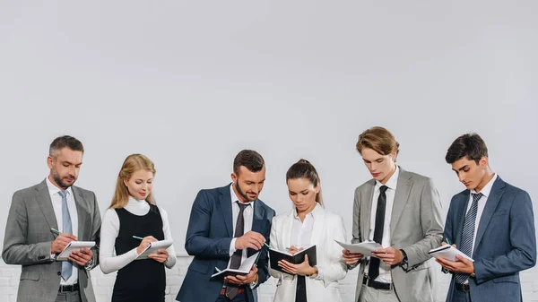 Businesspeople in formal wear standing in row and writing something to notebooks during training in hub — Stock Photo