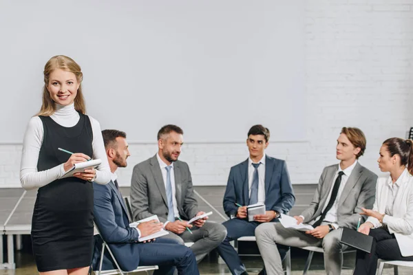 Hermoso entrenador de negocios de pie delante de los empresarios en la formación en el centro - foto de stock