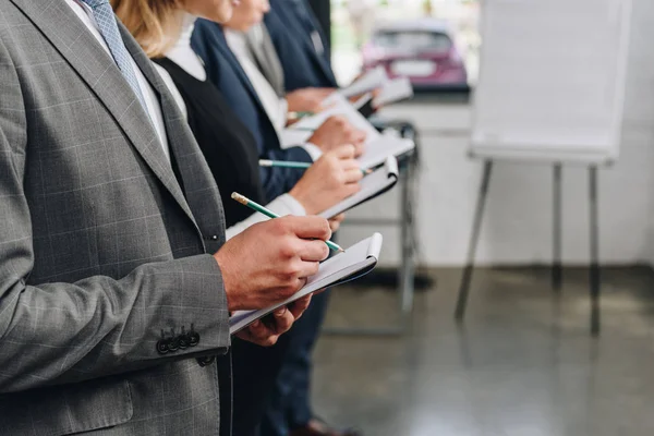 Cropped image of businesspeople standing in row and writing something to notebooks during training in hub — Stock Photo