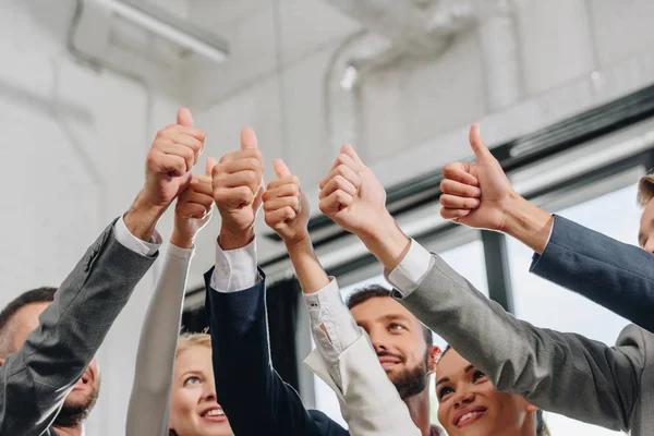Baixo ângulo de visão de empresários sorridentes mostrando polegares para cima no hub — Fotografia de Stock