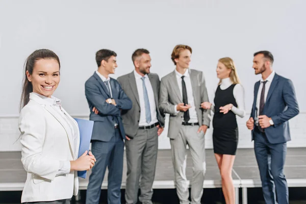 Sonriente entrenador de pie cerca de los empresarios en el centro y mirando a la cámara - foto de stock