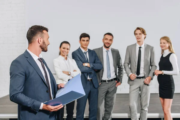 Entrenador de pie con portapapeles cerca de los empresarios en el centro - foto de stock