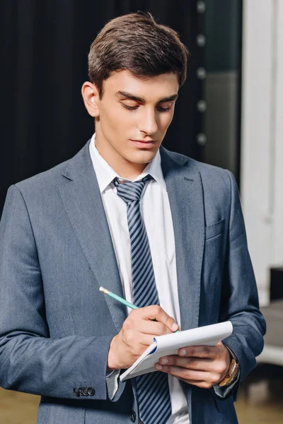 Guapo hombre de negocios escribiendo algo a cuaderno en el hub - foto de stock