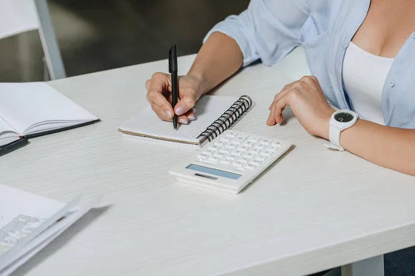 Cropped image of businesswoman writing something to notebook at table in office — Stock Photo