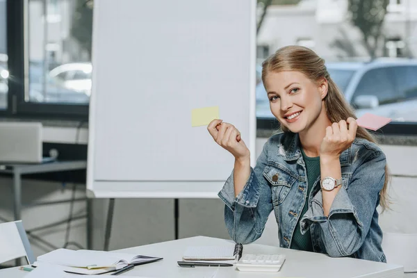 Atractiva mujer de negocios sonriente sosteniendo pegatinas de papel en la oficina — Stock Photo