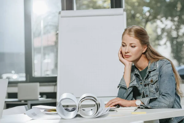 Tired beautiful businesswoman resting chin on hand at table in office — Stock Photo