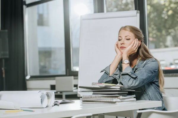 Müde Geschäftsfrau stützt Kinn auf Hände am Tisch im Büro — Stockfoto