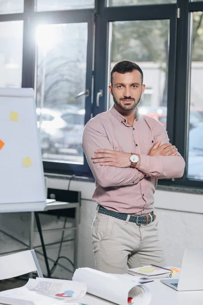 Handsome businessman standing with crossed arms and looking at camera in office — Stock Photo
