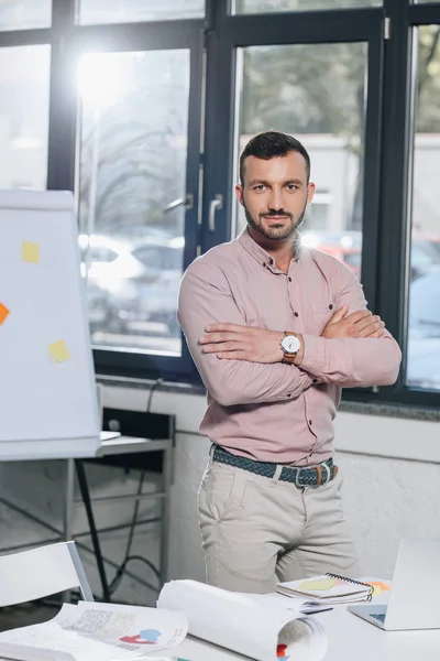 Bell'uomo d'affari in piedi con le braccia incrociate e guardando la fotocamera in ufficio — Foto stock