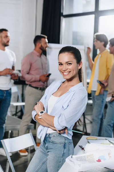 Lächelnde Geschäftsfrau mit verschränkten Armen blickt während eines Treffens im Büro in die Kamera — Stockfoto