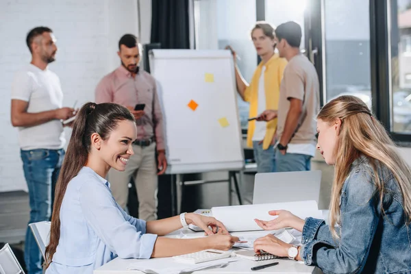 Smiling businesswomen looking at documents during meeting in office — Stock Photo