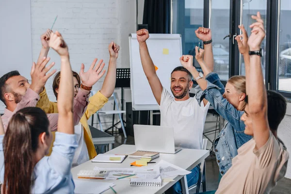 Happy businesspeople sitting with raised hands during meeting in office — Stock Photo